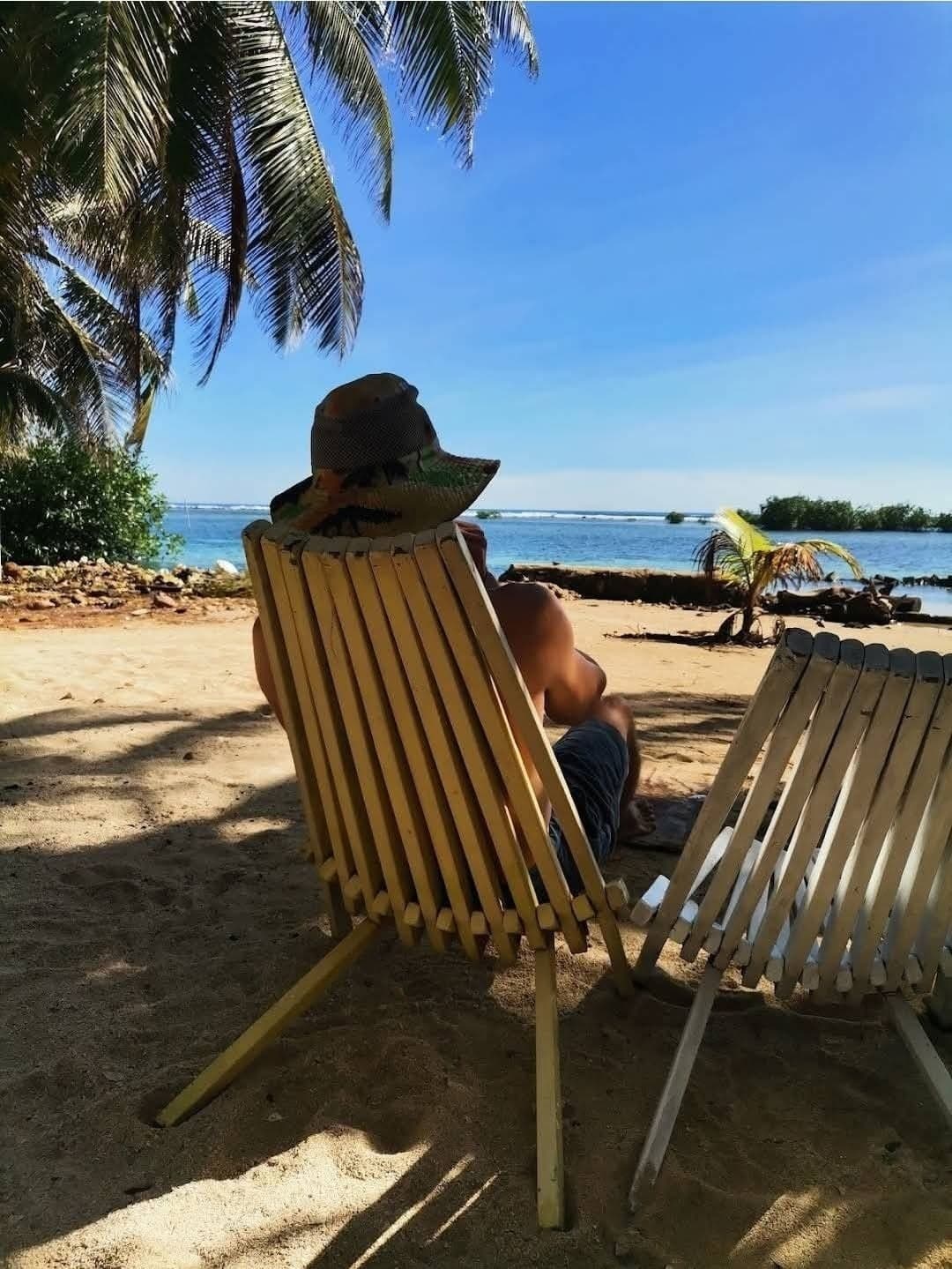 A person relaxing in a beach chair under palm trees, with a scenic view of the ocean.