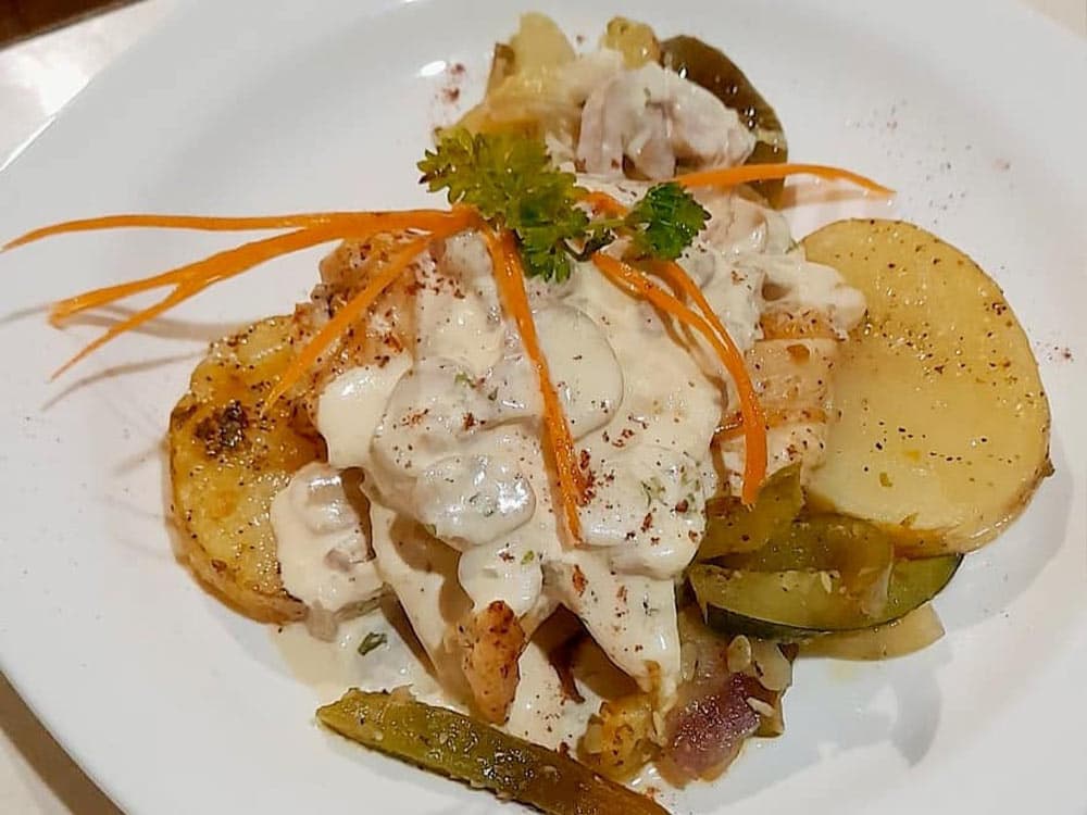 A plate of creamy chicken topped with herbs and garnished with carrot strips, served alongside roasted vegetables and potatoes.