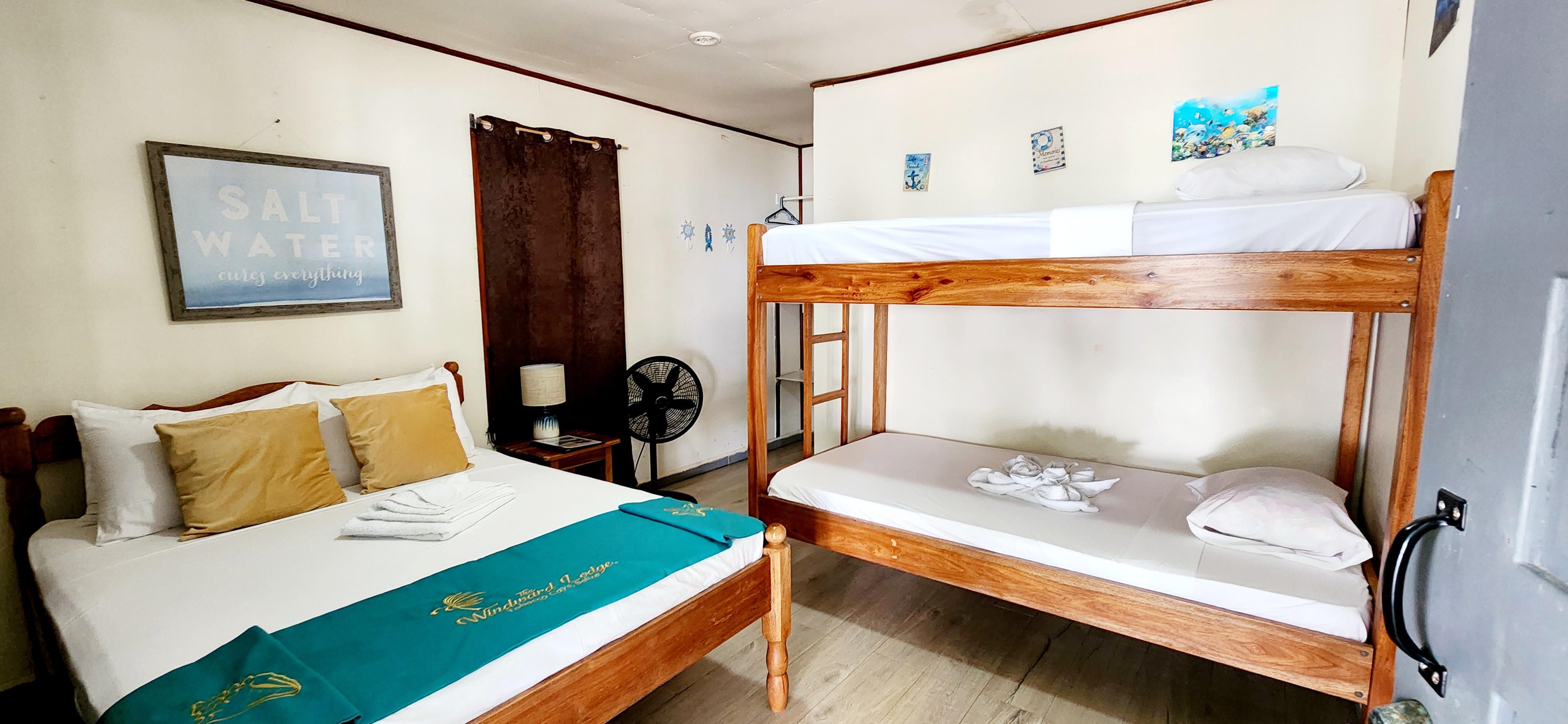A cozy room featuring a double bed and a bunk bed, with light wood furniture and beach-themed decor.