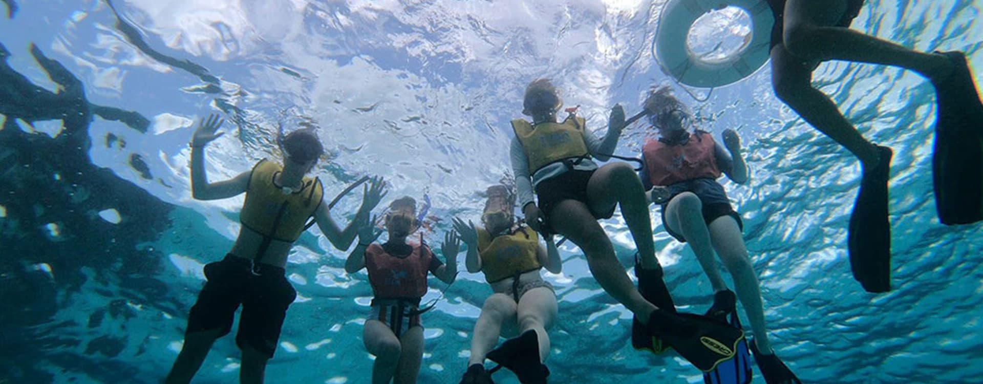 A group of snorkelers waves from beneath the water's surface.