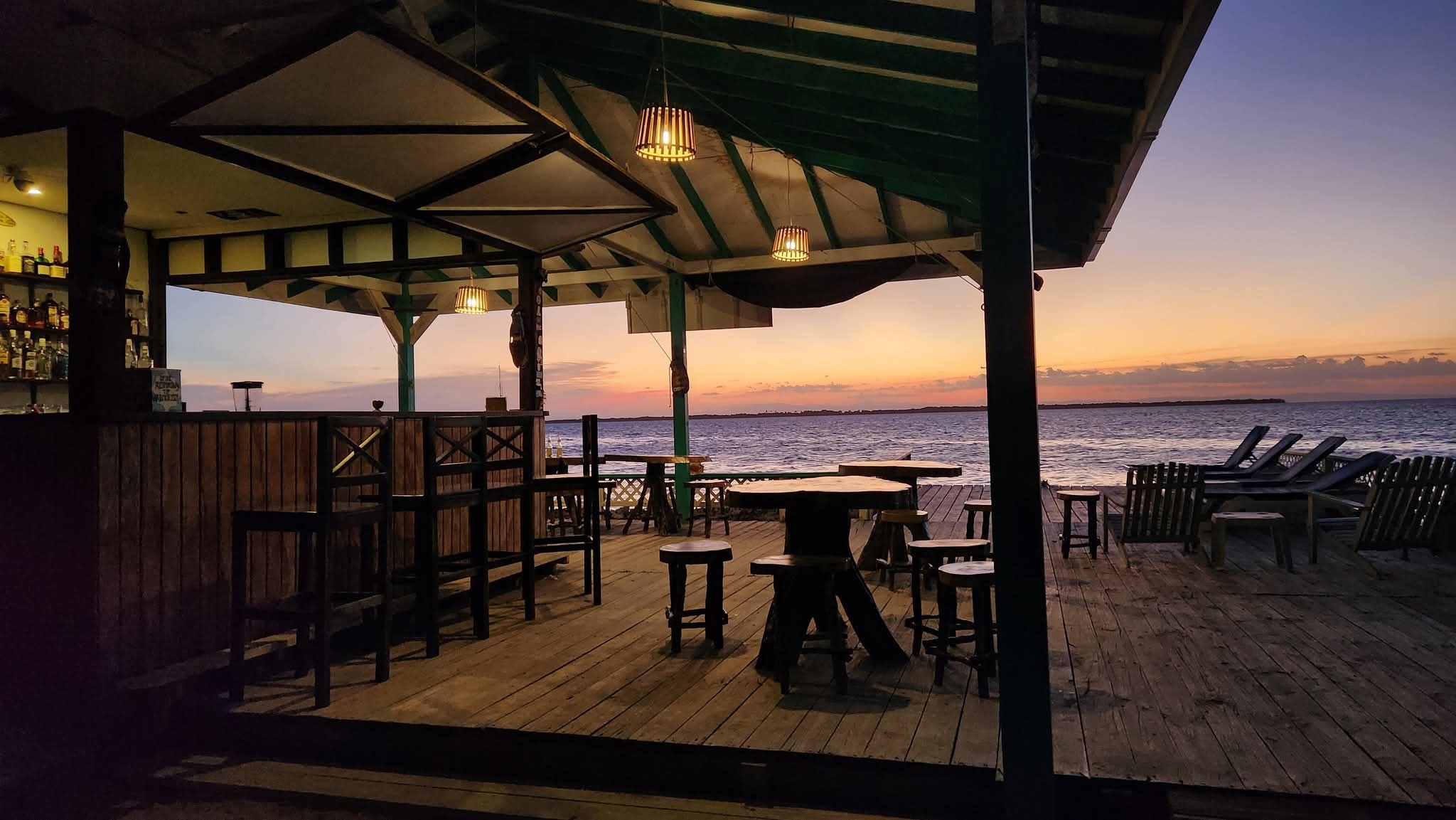 A sunset view from a seaside bar with wooden furniture and a calm ocean in the background.