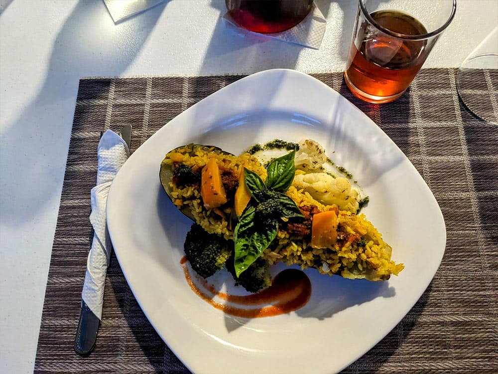 A plate of stuffed zucchini with vegetables and sauces, accompanied by a glass of dark beverage.