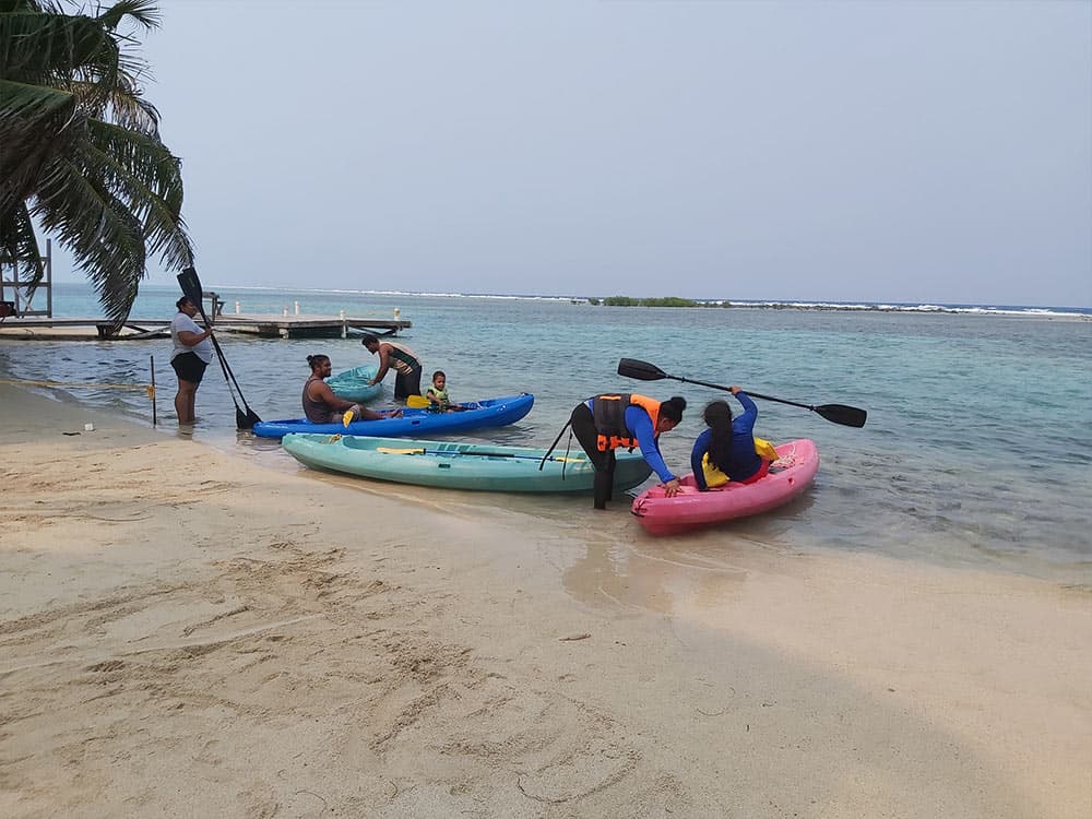 A group of people are preparing kayaks on a sandy beach by the water.