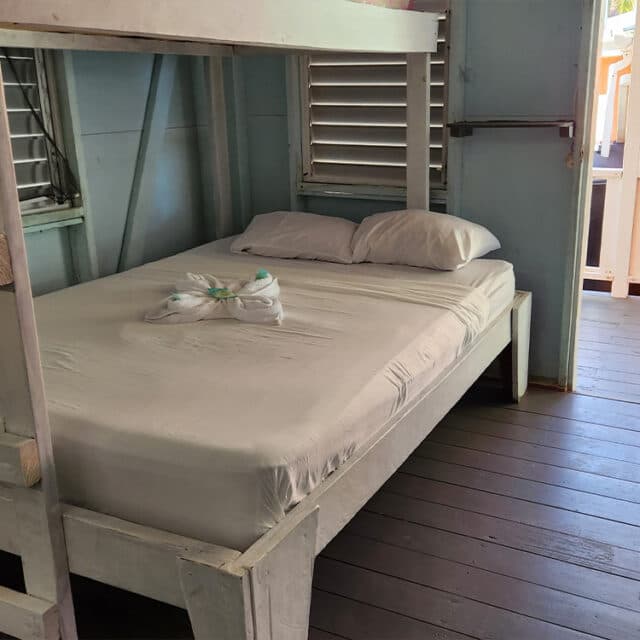 A simple, unmade bed with white sheets and pillows in a wooden, light blue room.