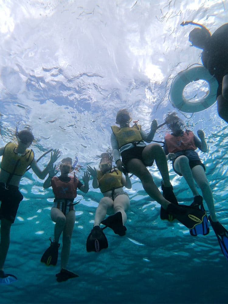 A group of people in snorkeling gear waves underwater.