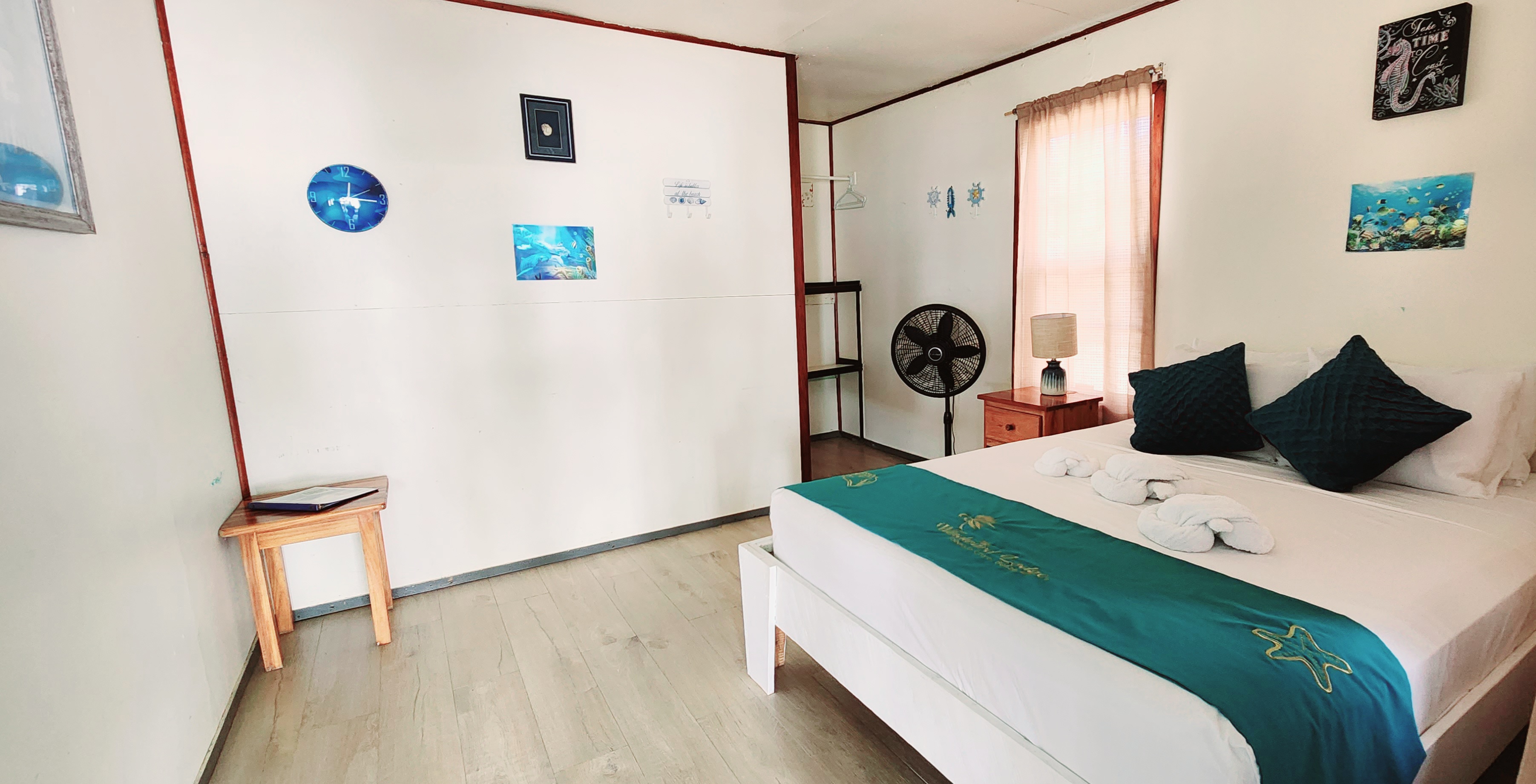 A cozy bedroom featuring a double bed, a small table, a fan, and decorative wall art.