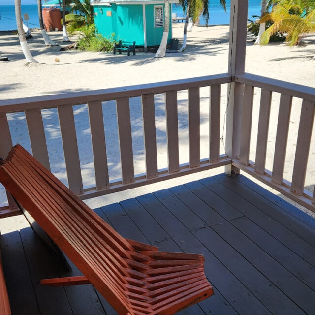 View from a porch featuring an orange lounge chair, overlooking a sandy beach and turquoise water.