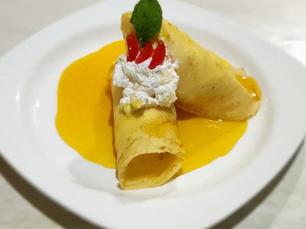 Two crepes drizzled with mango sauce, topped with whipped cream and a mint leaf.