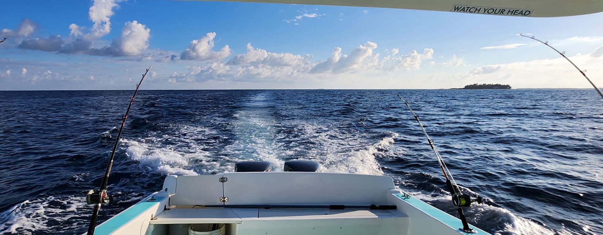 A boat navigates through open water with fishing rods set up against a backdrop of clouds and a distant island.