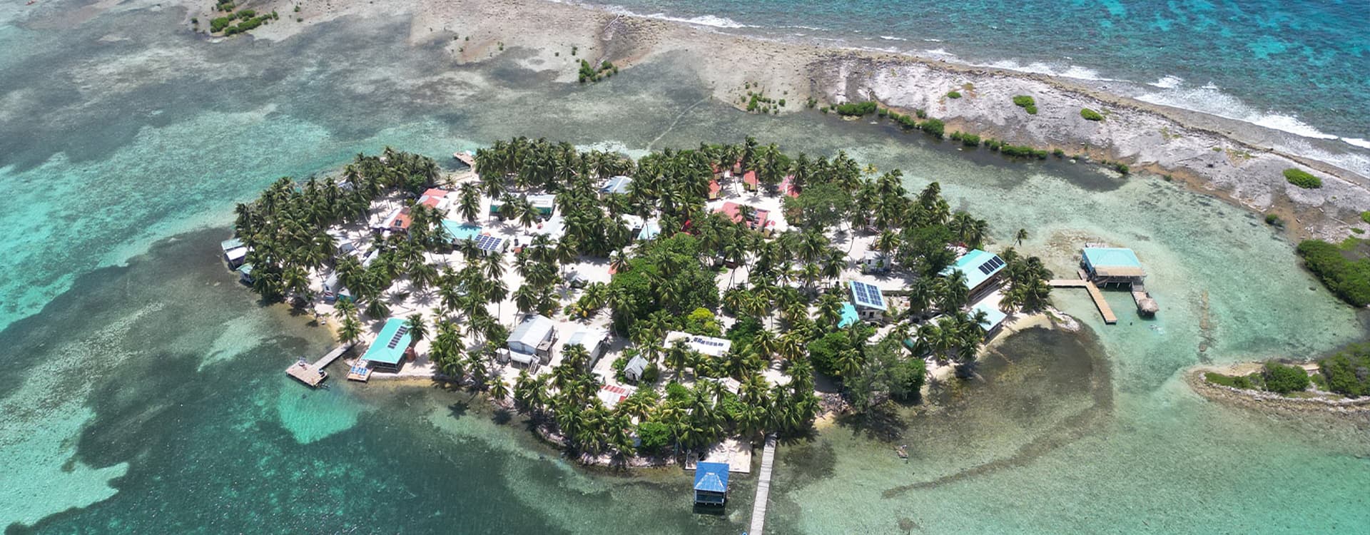 Aerial view of a tropical island with palm trees and colorful buildings surrounded by turquoise waters.