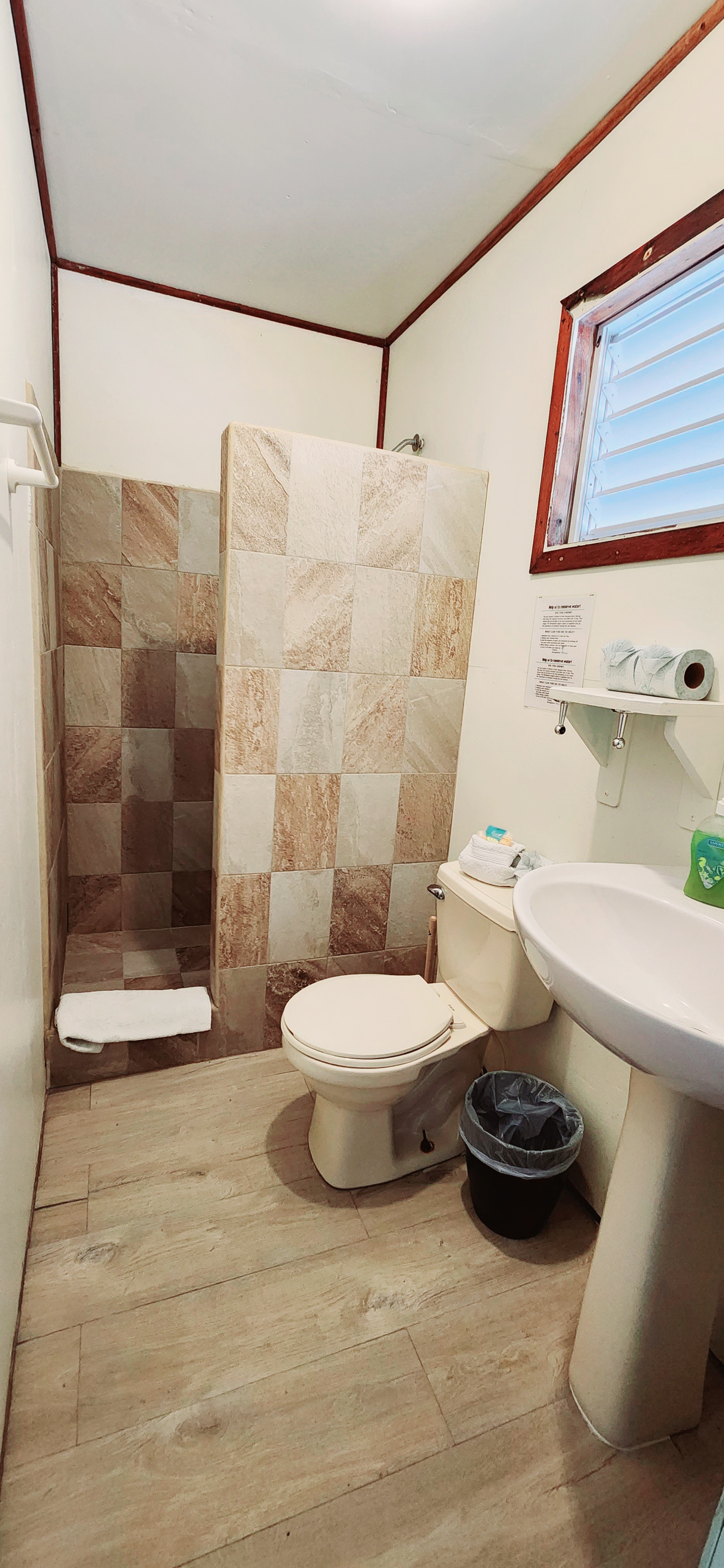 A small bathroom featuring a shower, toilet, sink, and wooden flooring.