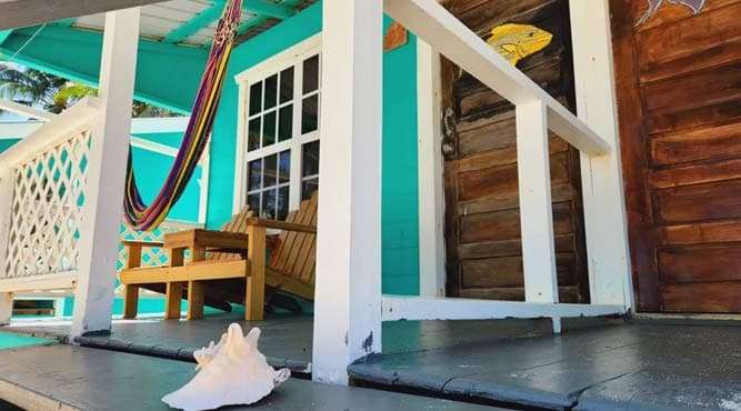 A shell rests on the porch of a colorful beach house with a hammock and wooden furniture.