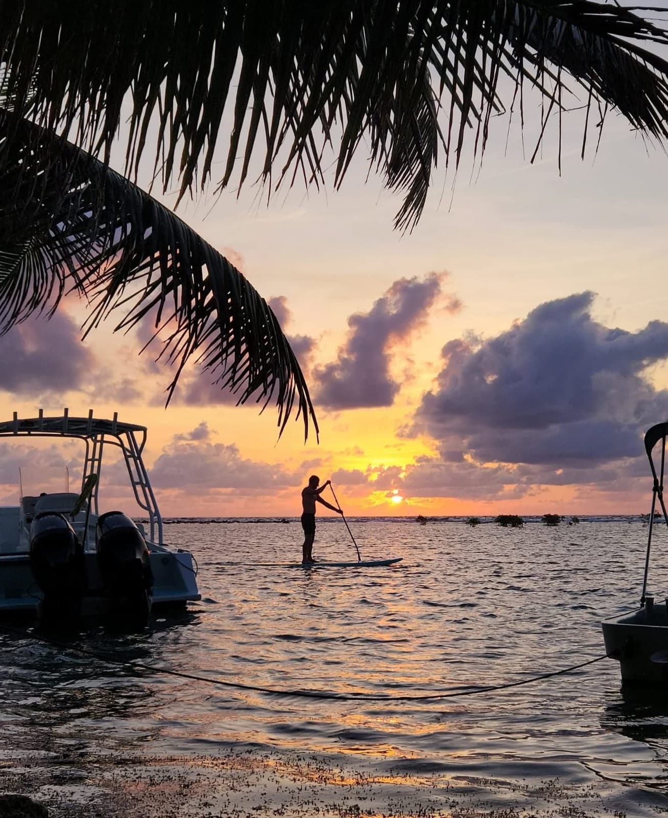 Silhouette of a paddleboarder against a vibrant sunset over the water.