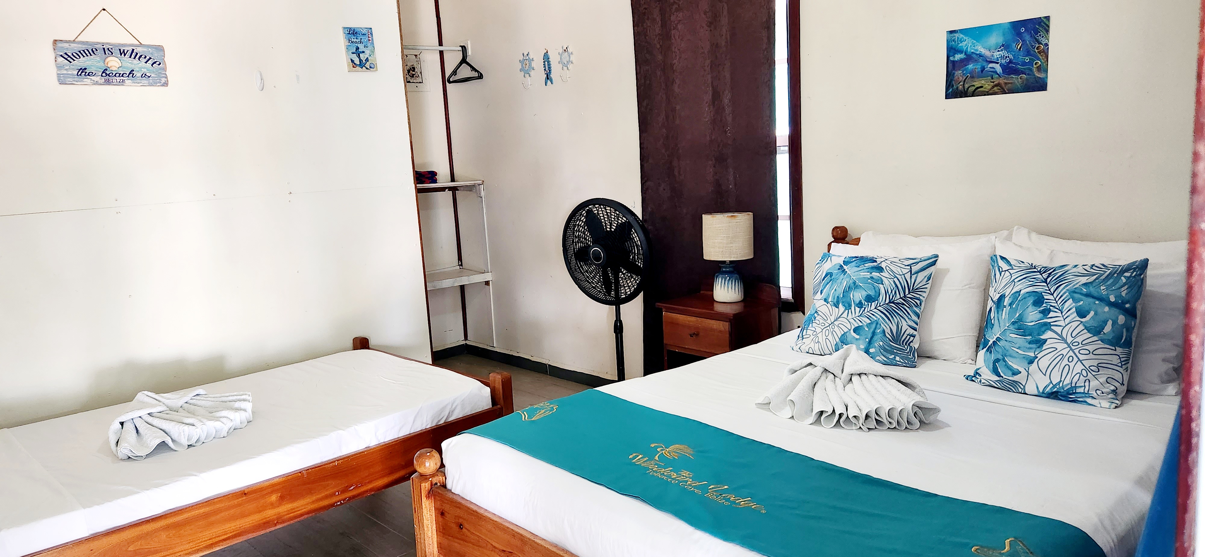 A cozy bedroom featuring two wooden beds, decorative pillows, a fan, and ocean-themed decor.