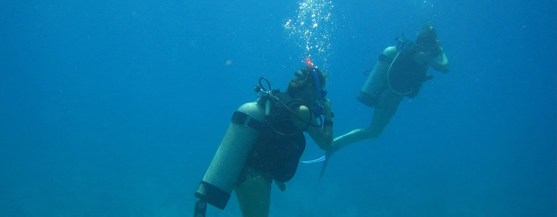 Two divers underwater, surrounded by blue water and bubbles.